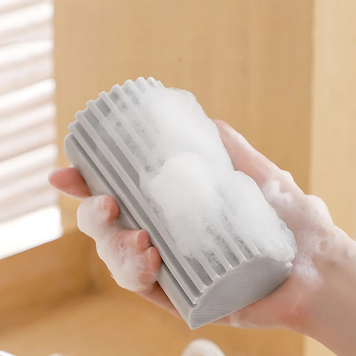 A gray ribbed sponge in hand, covered in soap suds.