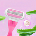 Close-up of a women's razor with a pink and white design, featuring multiple blades and a moisture strip, set against a pink background with aloe vera leaves.