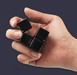 A single hand holding a partially unfolded black Crazy Cube against a dark background.