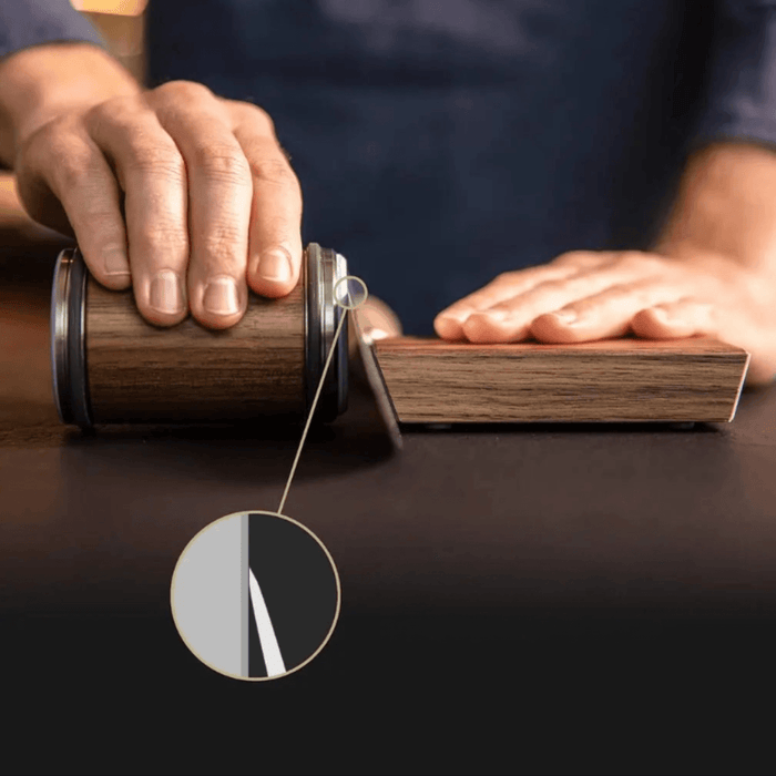 Close-up of hands using the wooden knife sharpener, emphasizing the blade's edge alignment.