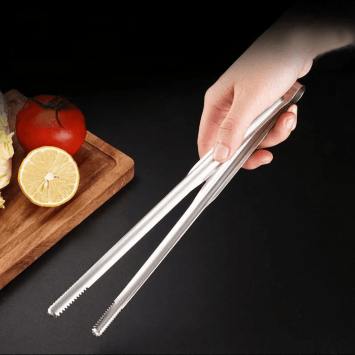 a hand holding the tongs, ready to use them to pick up food from a wooden cutting board, emphasizing their ergonomic design.