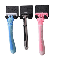 three razors with different colored handles—blue, black, and pink—each fitted with a textured black blade cover. The razors are wet, suggesting recent use or storage in a damp environment.