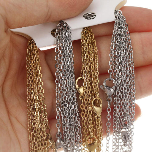 A hand displaying multiple strands of gold and silver stainless steel chains, showcasing their fine link design and lobster clasps.