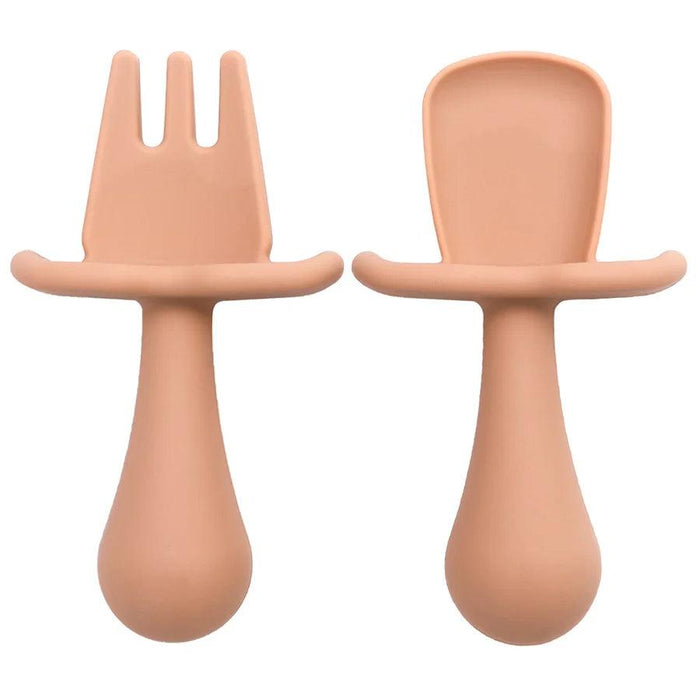 A close-up shot of two peach color silicone baby utensils, a fork and a spoon, showing their detailed design and texture.