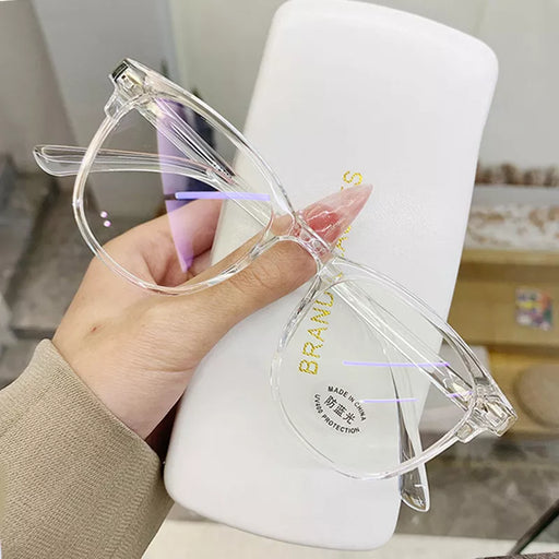 Clear-framed glasses held in front of a white case with gold lettering, showcasing a close-up view.