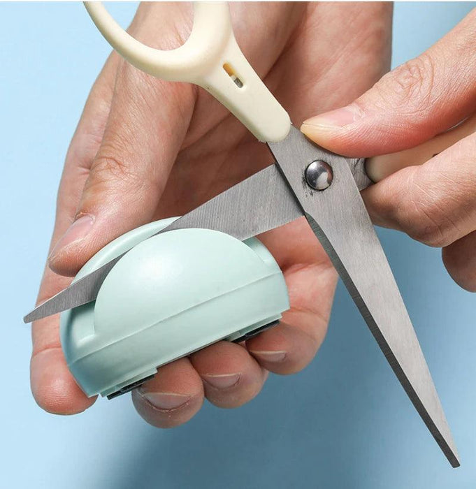 a person using a small, pale green sharpener to sharpen a pair of scissors, holding the sharpener in their hand.