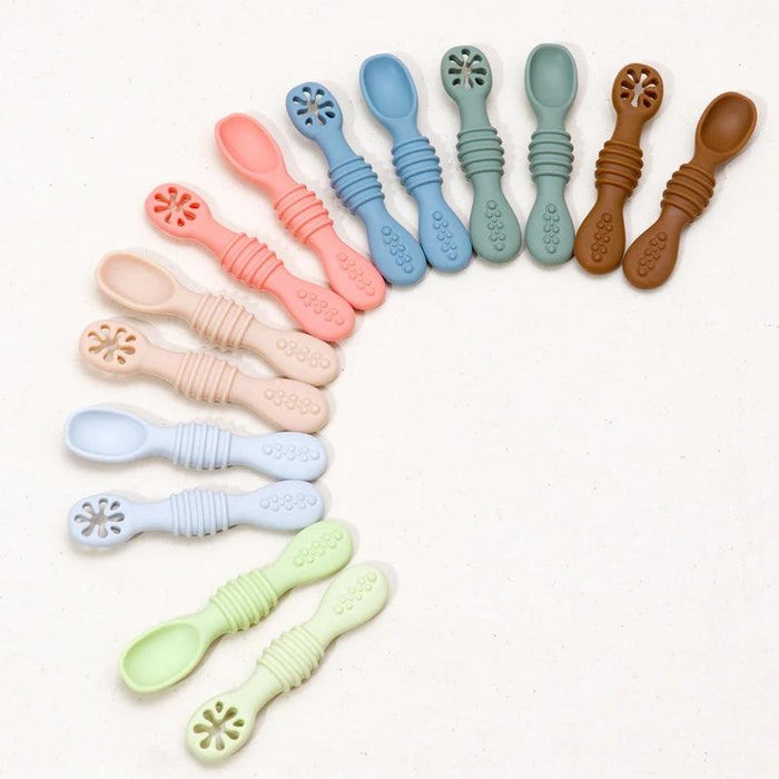 A rainbow arrangement of baby spoons in various pastel colors laid out in an arc pattern on a white background.