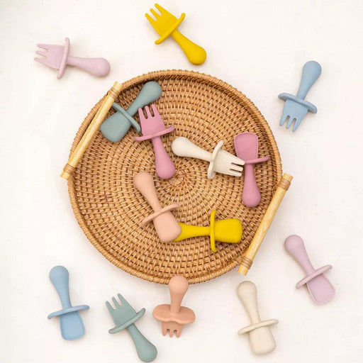 A variety of colorful baby utensils, including spoons and forks, placed in and around a woven basket.