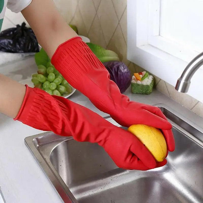 A person wears red cleaning gloves and holds a lemon in his hand above the sink, with purple cabbage, lettuce, grapes, and a blurred black trash bag appearing in the background.