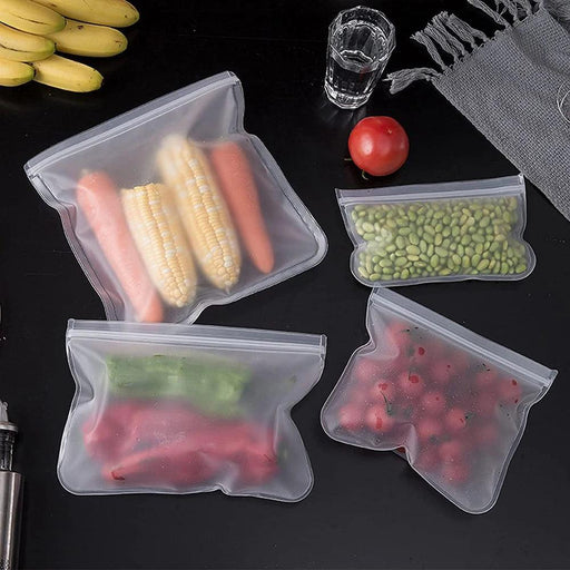 Reusable silicone food storage bags on a black table, containing corn, carrots, green beans, and cherries.