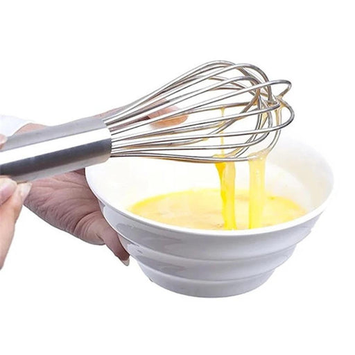 A hand is whisking an egg mixture in a white bowl using a stainless steel whisk. The image focuses on the action of mixing the eggs.