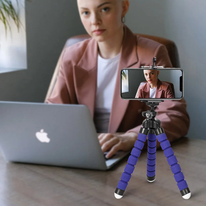 Woman using a flexible tripod to hold her phone while working on a laptop.