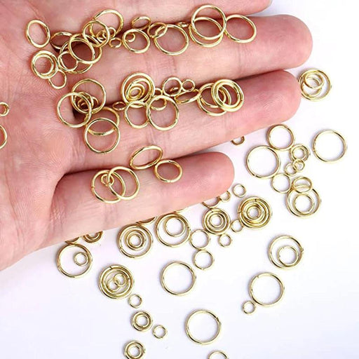 Assorted gold jump rings in various sizes, displayed on a hand and a white surface.