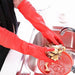 A person wears red cleaning gloves and holds food over the sink with a red strainer inside.