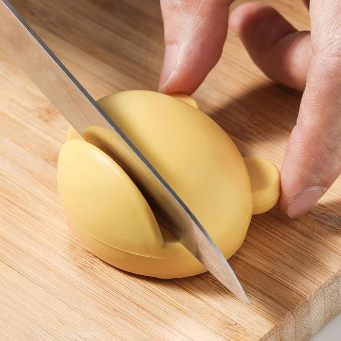 yellow, rounded knife sharpener on a wooden cutting board, with a knife being carefully sharpened by someone using it.