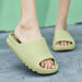 A close-up of a person's feet wearing light green slide sandals on a concrete surface, with a green background.