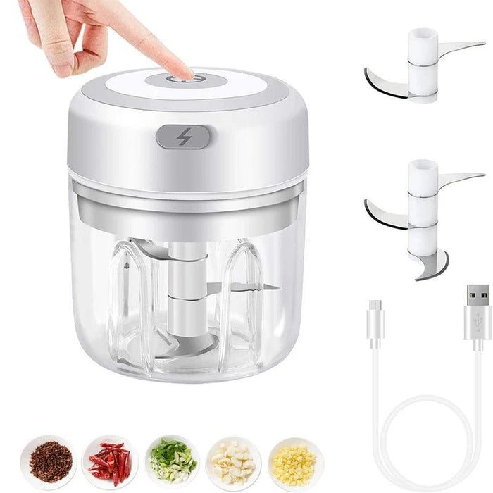 A food chopper with a finger pressing the top button, surrounded by additional blades, a USB cable, and bowls of chopped ingredients like garlic and chili.