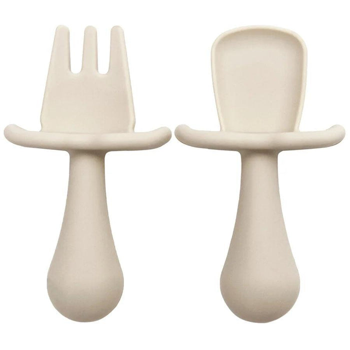 A close-up shot of two cream color silicone baby utensils, a fork and a spoon, showing their detailed design and texture.