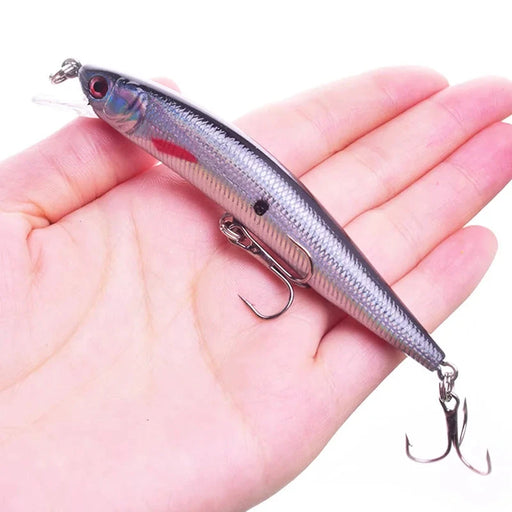 A hand holding the silver fishing lure to demonstrate its size and scale, showing the compact yet detailed design.