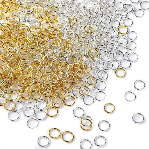 A mix of gold and silver jump rings in different sizes, scattered on a white surface.