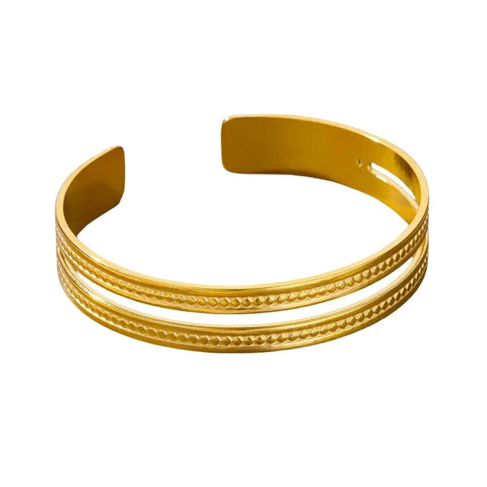 Gold cuff bracelet with two parallel etched lines, displayed on a white background.