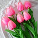 A bunch of seven artificial pink tulips with vibrant green leaves, arranged on a white decorative plate.