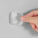 A clear square silicone bumper pad is being pressed onto a smooth surface by a person's thumb.