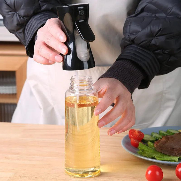 A person holding a black oil spray bottle, refilling it with oil.