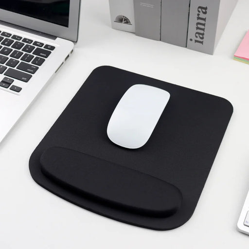 A black ergonomic mouse pad with a white mouse, placed next to a laptop and books, displayed on a white desk background.