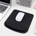 A black ergonomic mouse pad with a white mouse, placed next to a laptop and books, displayed on a white desk background.