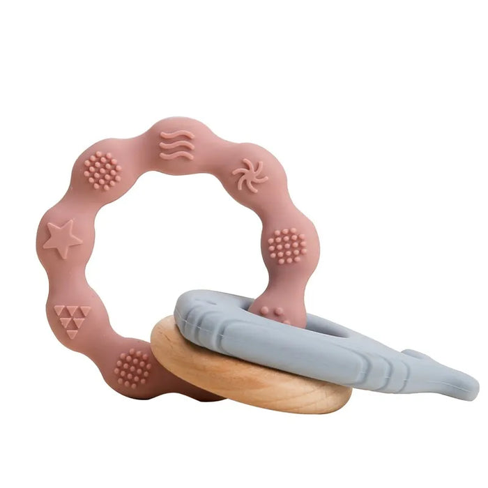 A pink silicone teether ring with blue various textured patterns and a wooden ring attached to it.