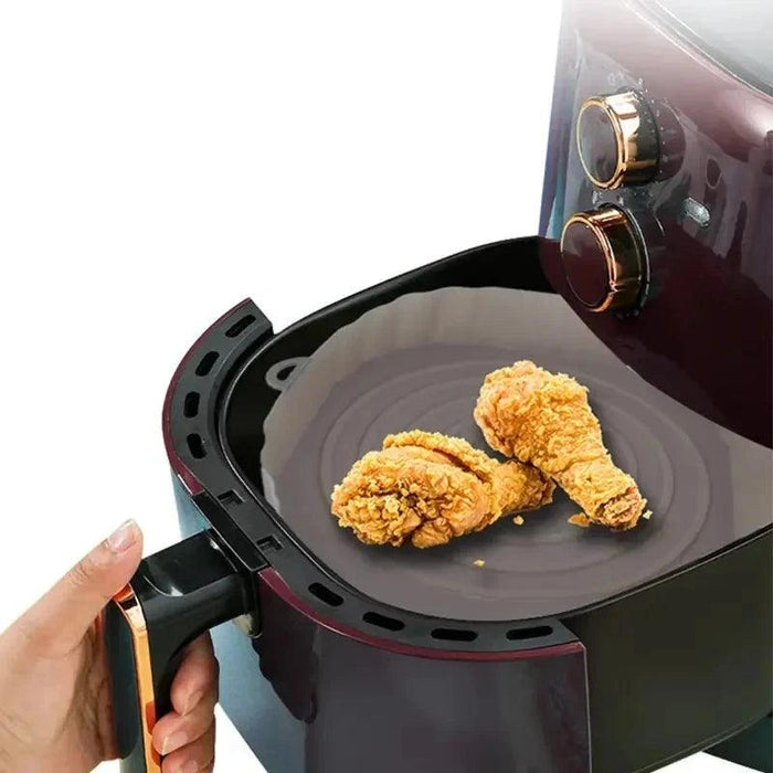 A hand holding an air fryer basket with a black silicone liner inside, containing two pieces of fried chicken.