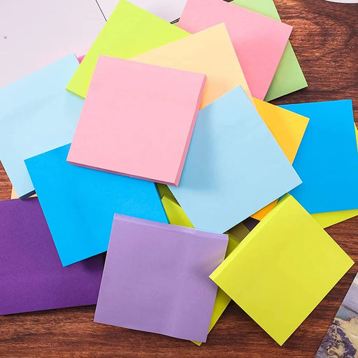 Assorted colorful adhesive note pads scattered randomly on a wooden background, featuring shades of pink, blue, yellow, green, and purple.