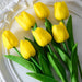 A bunch of vibrant yellow tulips with green leaves on a white plate.