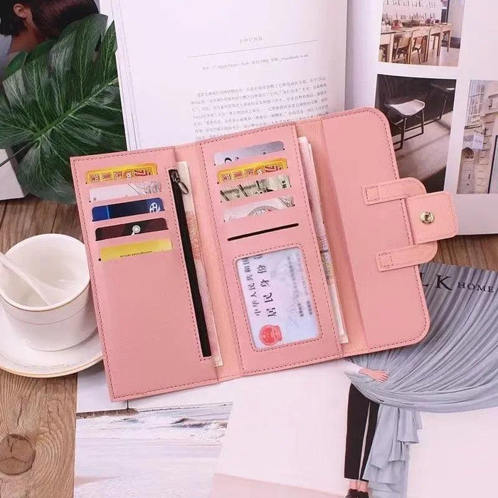 An open pink wallet laid flat on a table, showing various card slots, a zippered compartment, and an ID window. The background includes an open book and a cup of coffee.