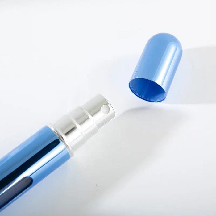 A close-up of a blue portable perfume spray bottle with the cap removed, showing the spray nozzle.