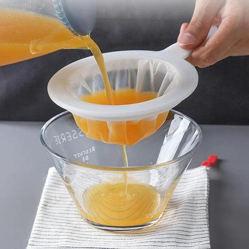 A person is pouring orange juice through a white strainer into a glass bowl, with the juice being filtered into the bowl.