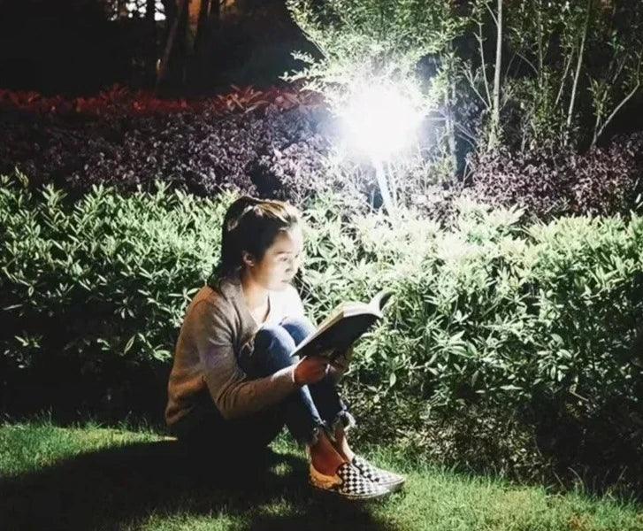 A person reading a book outdoors at night, illuminated by the LED camping lantern.