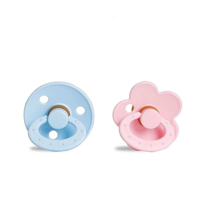 A round, blue pacifier with a ring handle next to a pink, flower-shaped pacifier with a ring handle.