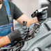 A close-up image shows a mechanic working on a vehicle. The mechanic is wearing black gloves and handling electrical connectors, demonstrating the protective nature of the gloves in a hands-on work environment.