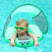 A toddler wearing green goggles, using a green baby float with a sunshade in a pool.