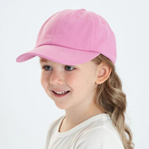 A young girl wearing a pink cap, smiling and looking to the side.