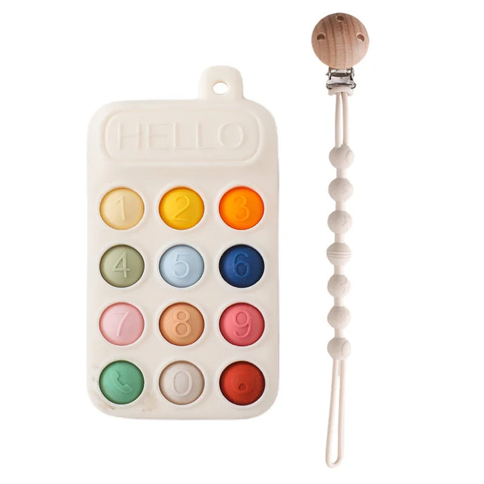 A cream silicone teether resembling a phone keypad with colorful buttons, next to a pacifier clip with a wooden clasp and pink silicone beads.