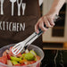 Person using stainless steel tongs to serve salad from a bowl.