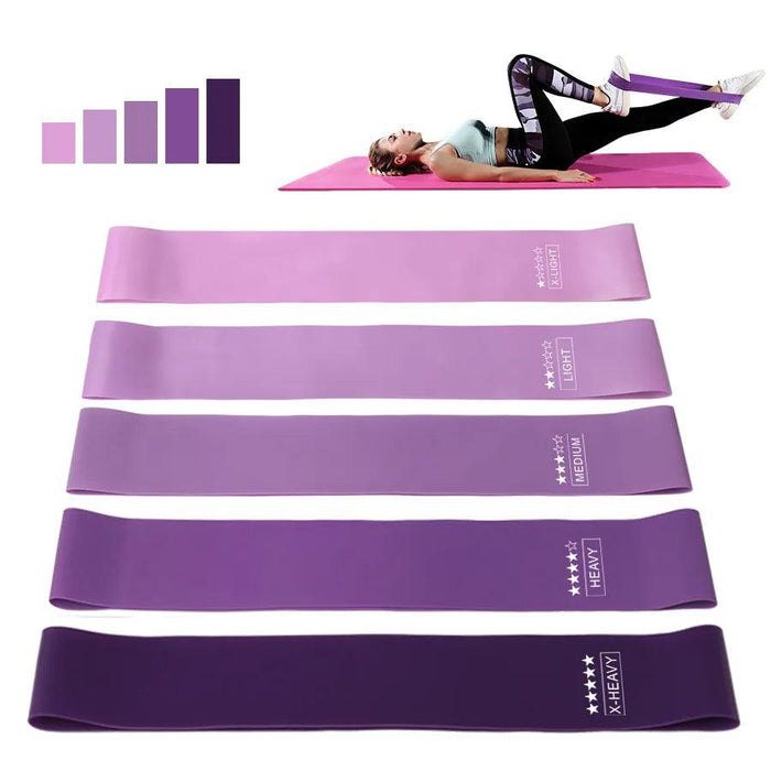 A woman lying on a pink yoga mat, using a purple resistance band to exercise her legs, with a gradient color bar indicating resistance levels.