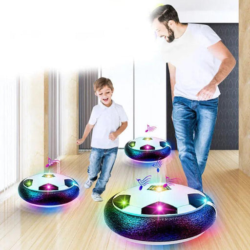 A man and a young boy playing with multiple hover soccer balls in a brightly lit indoor hallway.