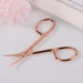 Rose gold Cuticle Scissors display on cream background with pink flower on top of the image.