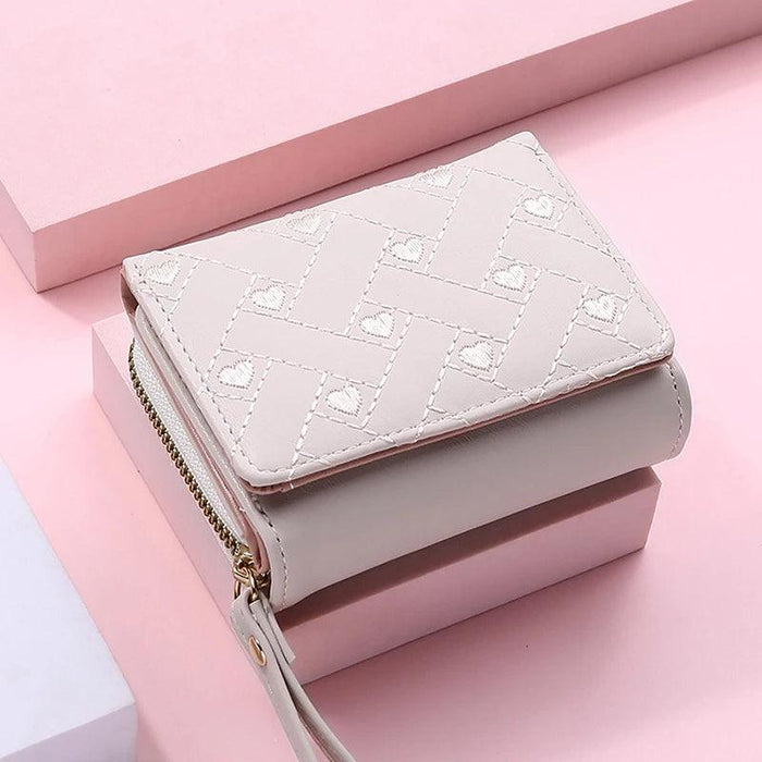 Closed beige wallet with a quilted pattern and a wrist strap, displayed on pink blocks.