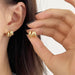 a woman wearing a pair of gold double hoop earrings. The design is chunky and elegant, adding a stylish touch to her look. The earrings are being held up close to her ear for a better view.