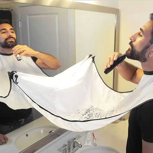 A man trimming his beard over a sink, with a white beard trimming bib attached to the mirror.